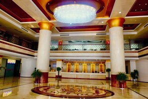 A hotel lobby with a grand chandelier, multiple columns, and a reception desk.