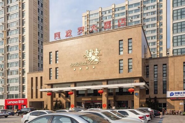 A hotel with a prominent sign, multiple floors, and a parking lot with cars. - Apollo Hotel (Yucheng)