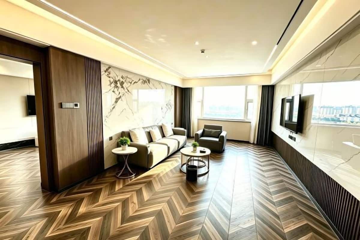 A modern hotel room with a herringbone floor pattern, a sofa set, a coffee table, and a TV mounted on the wall.