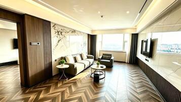 A modern hotel room with a herringbone floor pattern, a sofa set, a coffee table, and a TV mounted on the wall.
