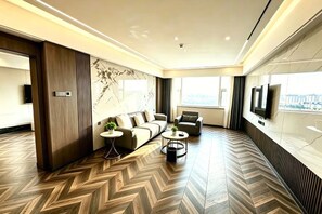 A modern hotel room with a herringbone floor pattern, a sofa set, a coffee table, and a TV mounted on the wall. - Apollo Hotel (Yucheng)