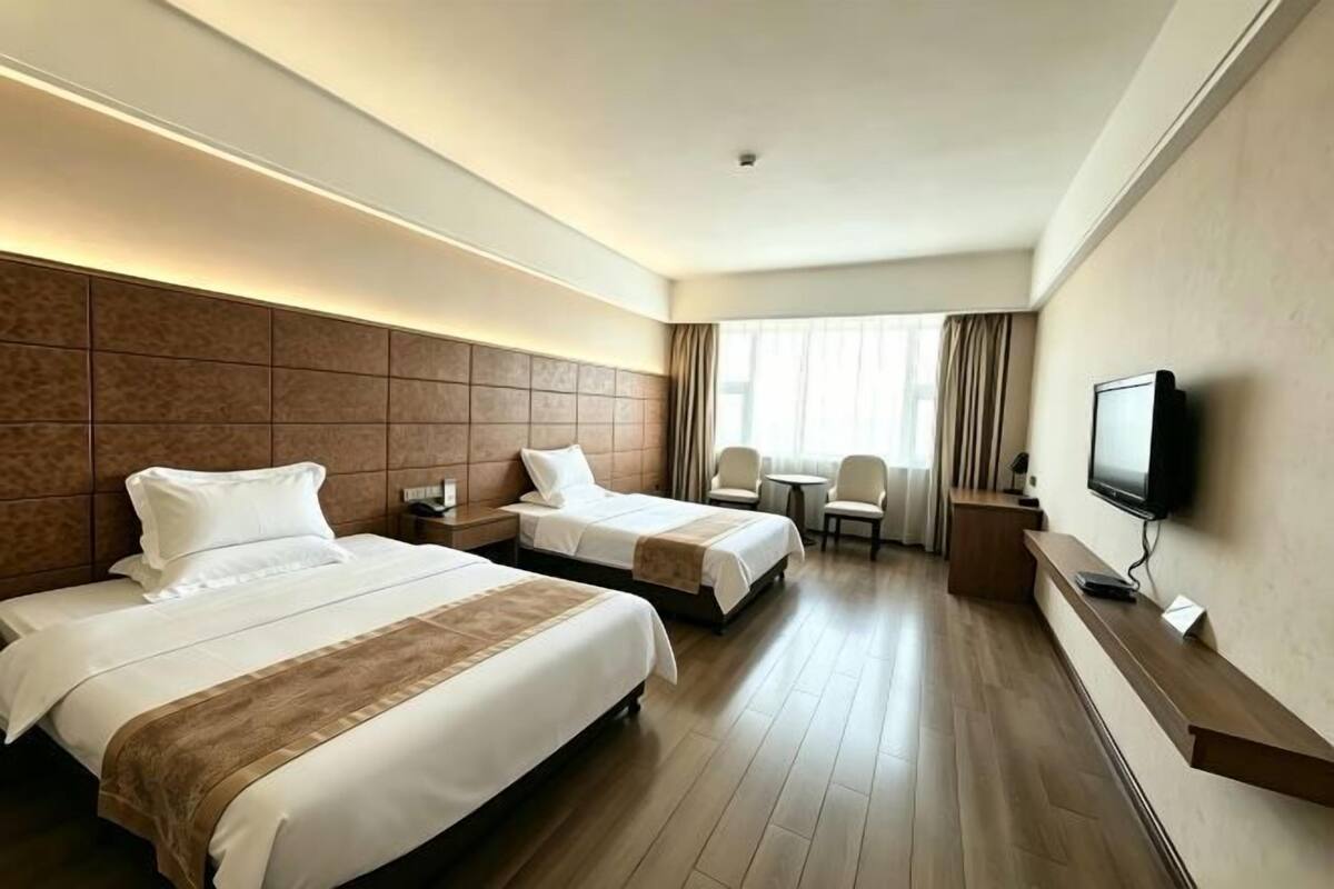 A hotel room with two beds, a TV, a desk, and a chair.