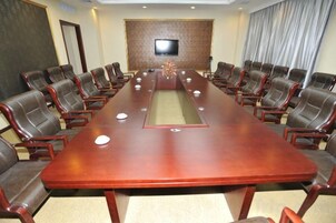 A conference room with a long table, multiple chairs, a television on the wall, and a curtain.