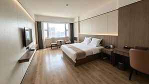 A modern hotel room with a large bed, a desk, a chair, a TV, and a view of the city. - Apollo Hotel (Yucheng)