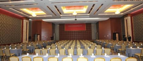 A conference room with rows of tables and chairs, a large screen at the front, and a patterned wall.