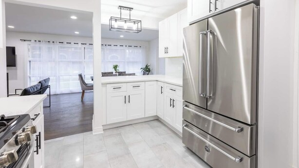Una cucina moderna con mobili bianchi, un frigorifero in acciaio inossidabile e un'area pranzo con un divano grigio.