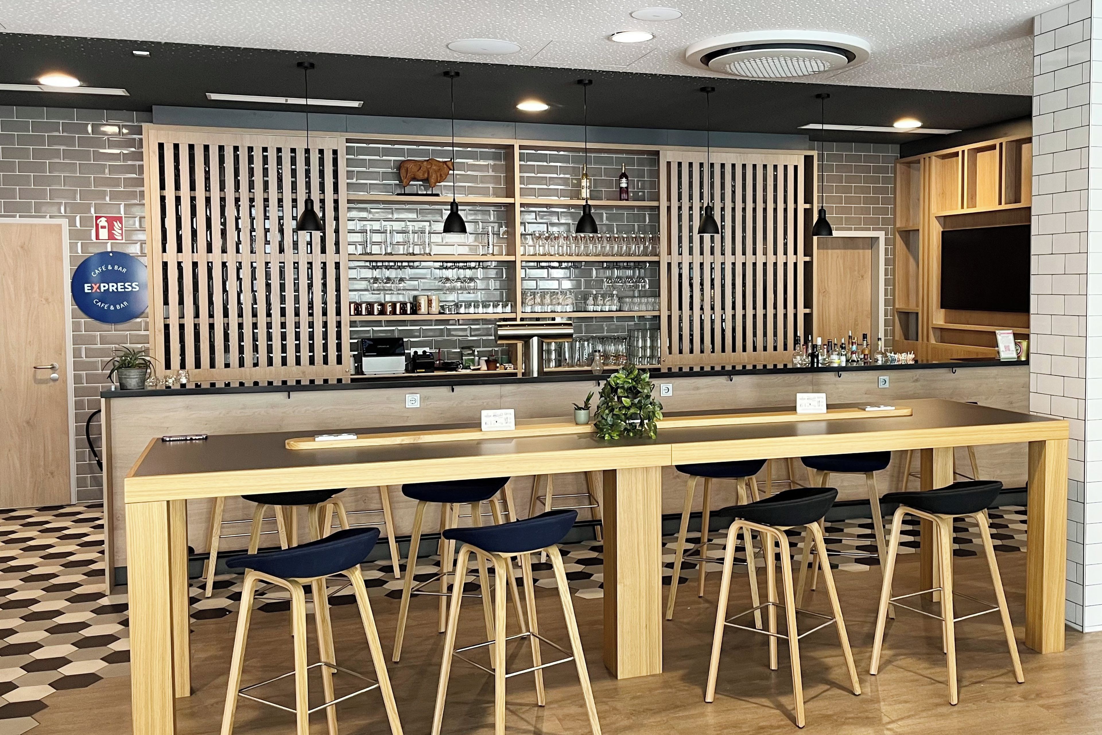 Eine Bar mit einer langen Theke, mehreren Barhocker und Regalen voller Gläser und Flaschen.