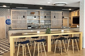 A bar area with a long counter, multiple stools, and shelves with glasses and bottles. - Holiday Inn Express Munich Airport - Erding by IHG (Erding)