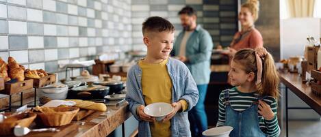 A breakfast buffet with various food items and a family interacting.