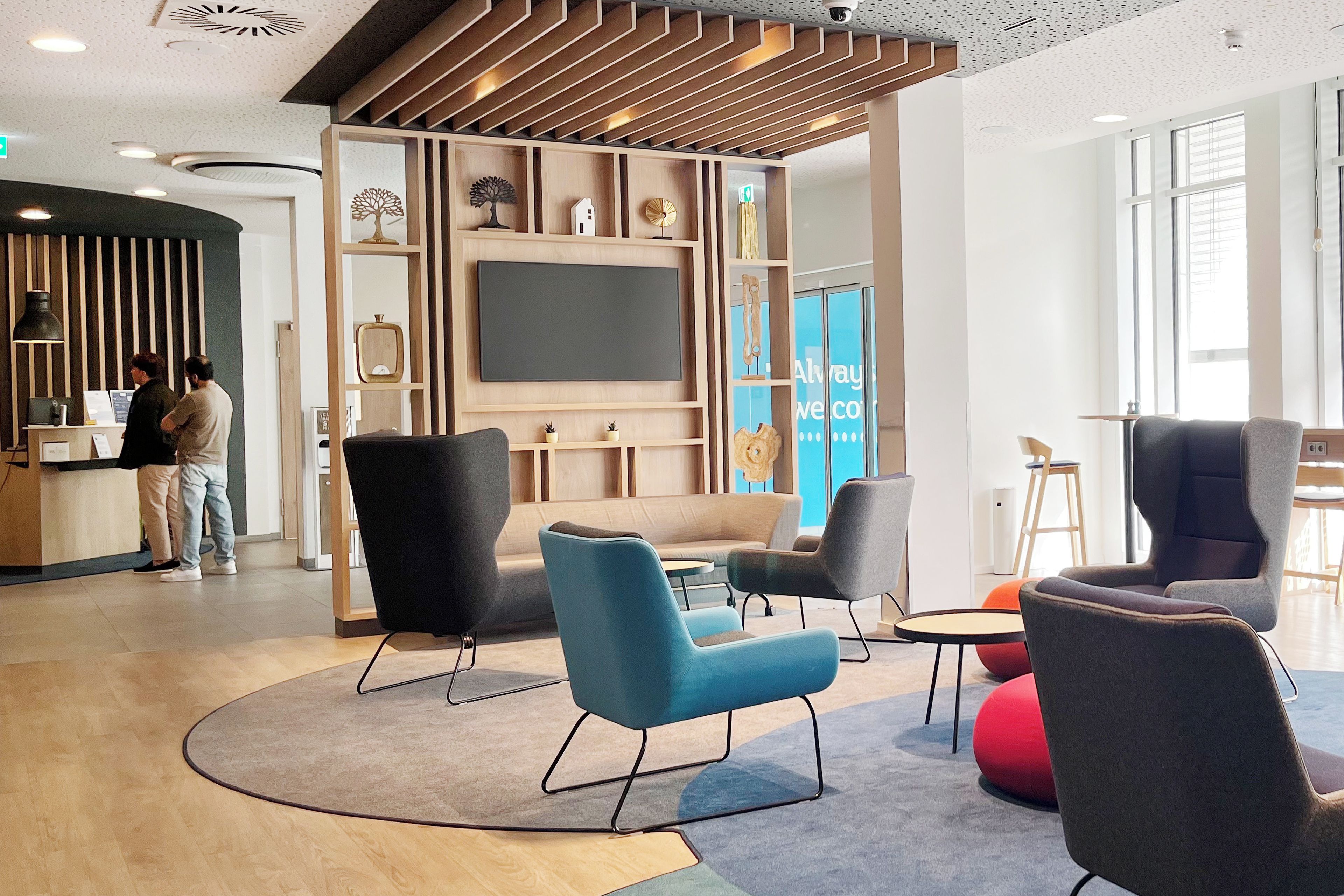 A modern lounge area with a reception desk, seating, and a large flat-screen TV.