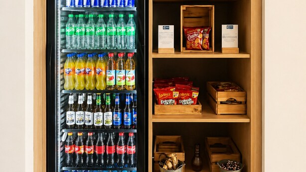 A vending machine stocked with various beverages and snacks, surrounded by wooden shelves with packaged goods. - Holiday Inn Express Munich Airport - Erding by IHG (Erding)