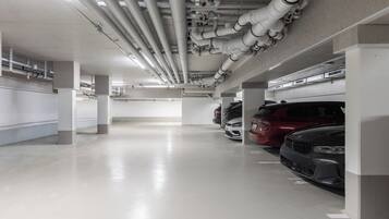 Un estacionamiento de varios niveles con pilares de hormigón, tuberías elevadas y varios automóviles estacionados.