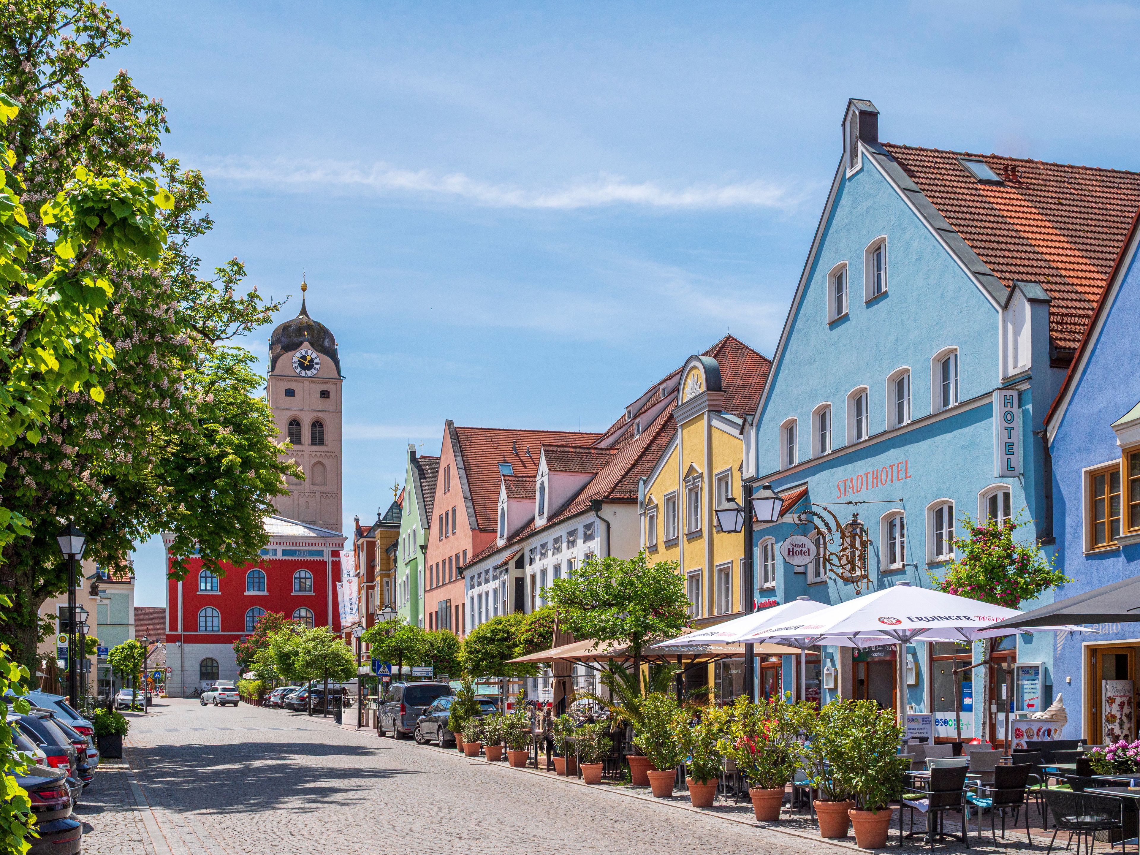 A cobblestone street lined with colorful buildings, including a hotel with outdoor seating.