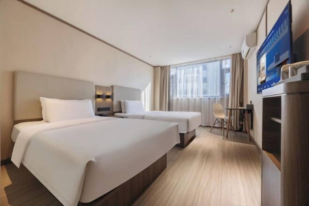 A hotel room with two beds, a desk, a chair, a TV, and a window with curtains.