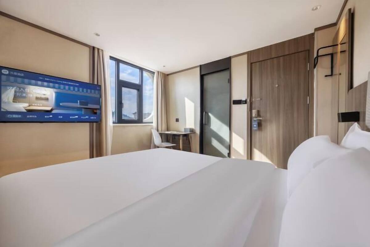 A hotel room with a bed, a TV mounted on the wall, a window, and a door.