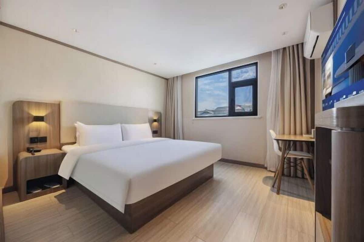 A hotel room with a large bed, bedside tables, a desk, and a window.