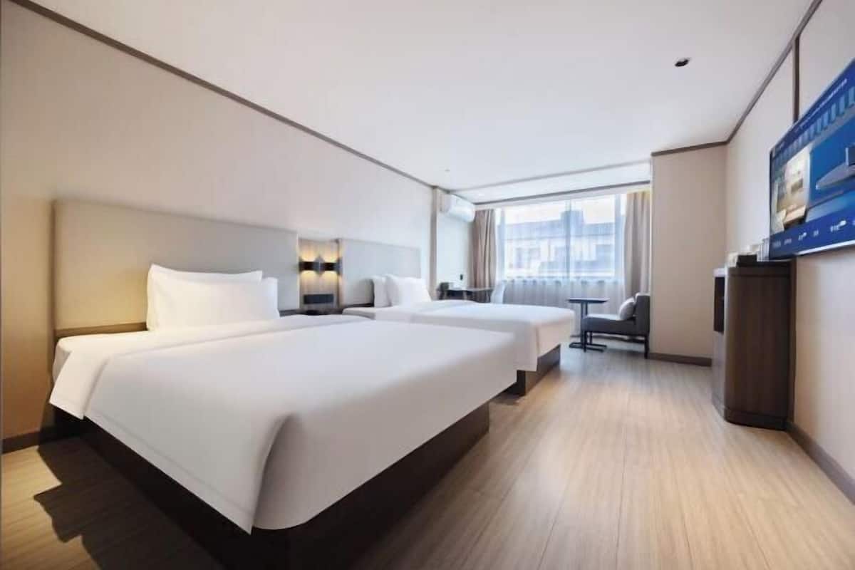 A hotel room with two beds, a desk, a chair, and a TV.