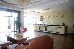 Un hall d’hôtel comprenant un comptoir d’accueil, des fauteuils en cuir, un lustre et de grandes fenêtres.