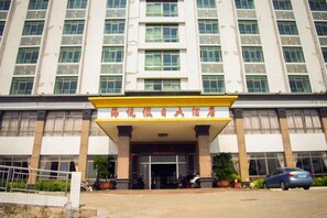 A multi-story building with a prominent entrance, a covered area with columns, and a parking lot with vehicles. - Haiyue Holiday Hotel (Yangxi)