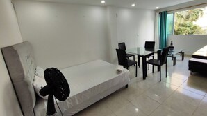 A modern hotel room with a single bed, a small table with chairs, a fan, and a view of greenery through a window. - EM3-1 APARTAMENTO 1 HAB ZONA RESIDENCIAL (Cartagena)