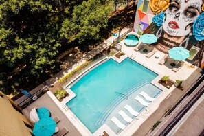 Una piscina en la azotea con un mural, sillas de descanso y sombrillas.