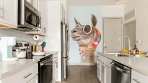 A modern kitchen with white cabinets, stainless steel appliances, and a large wall mural of a llama.