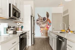 Een moderne keuken met witte kasten, roestvrijstalen apparatuur en een groot wanddecoratie van een lama.
