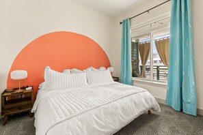 Un dormitorio con una cama grande, una mesita de noche con lámpara y una ventana con cortinas.