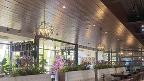 Een modern restaurantinterieur met een lange toonbank, beklede zitjes, rieten stoelen en hangende pendellampen.