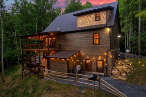 A two-story log cabin with a deck, outdoor lighting, and a stone wall.