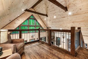A spacious loft bedroom with a sloped ceiling, large windows, and a balcony with a wooden railing. - Cabin· Pool·Hot Tub·Sauna·Creek·Sleeps 12 (Sevierville)