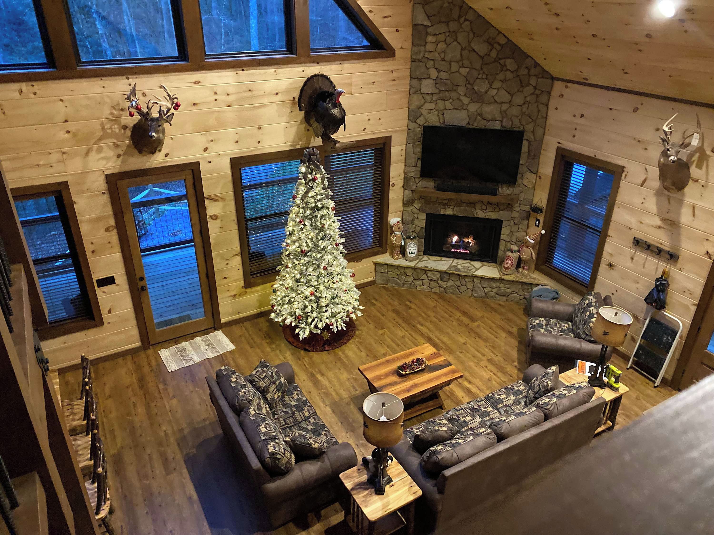 A cozy cabin interior with a fireplace, a Christmas tree, and a stone wall.