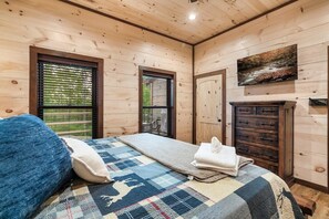 A wooden-paneled room with a bed, a fireplace, and a painting on the wall. - Cabin· Pool·Hot Tub·Sauna·Creek·Sleeps 12 (Sevierville)