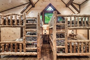 Eine Holzhütte mit Etagenbetten, die in einem zentralen Gang angeordnet sind, einem kleinen Tisch mit einer Laterne und einem Fenster mit Blick auf Grünflächen.