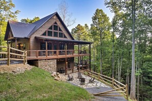 Eine zweistöckige Lodge mit Steinfundament, Holzterrasse und einem überdachten Sitzbereich im Freien.