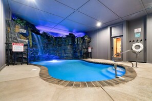 A swimming pool with a waterfall feature, surrounded by a stone wall and a lifeguard stand.