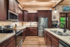 Eine Küche mit dunklen Holzausziehtüren, Edelstahlgeräten, Granit-Arbeitsplatten und einem Holzboden.