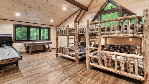 A room with a sloped ceiling, wooden bunk beds, a table, and a window with a view of greenery. - Cabin·Indoor Pool·Sauna·Game Rm·Creek·15 Min to NP (Sevierville)