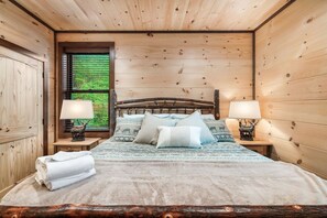 A wooden-paneled room with a bed, two nightstands, and a window with blinds. - Cabin· Pool·Hot Tub·Sauna·Creek·Sleeps 12 (Sevierville)