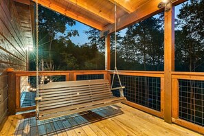 A wooden deck with a swing, metal railing, and a view of trees.