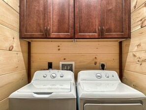 A laundry area with two white front-loading washers and a wooden cabinet above.