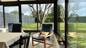Un invernadero con una mesa de comedor, dos sillas y vistas a un jardín.
