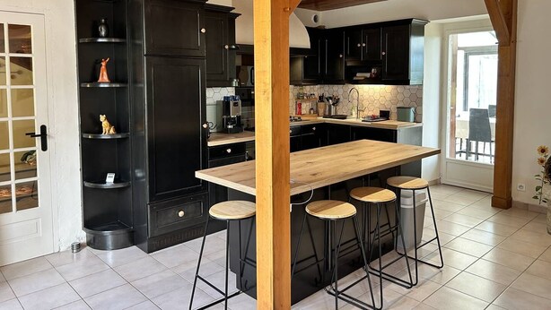 Una cocina moderna con armarios negros, una isla de madera con taburetes altos y un salpicadero con azulejos hexagonales.