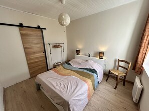 Ein Schlafzimmer mit einem Bett, Nachttischlampen, einem Holzstuhl, einem Heizkörper und einer Hängelampe.
