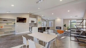Un vaste espace de vie comprenant une table à manger, des chaises blanches, un coin cuisine équipé d’appareils électroménagers modernes et un escalier menant à un autre niveau.
