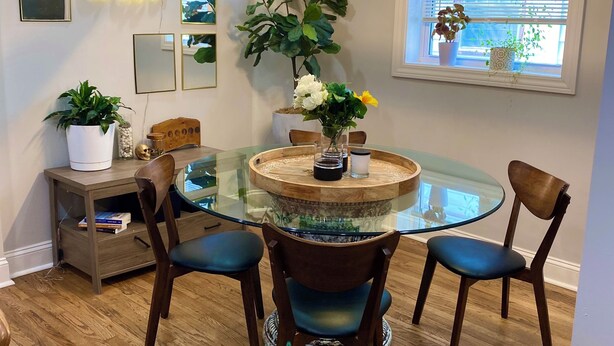 Een eethoek met een tafel met glazen blad, vier stoelen en een hanglamp.