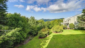 A residential property with a well-maintained lawn, a wooden deck, and a mountain backdrop. - Close to Hiking & Town! Peaceful Sugar Mtn Condo (Sugar Mountain)