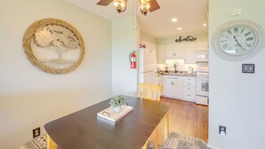 A dining area with a dark wooden table, a decorative tree wall art, a ceiling fan, and a kitchen in the background. - Close to Hiking & Town! Peaceful Sugar Mtn Condo (Sugar Mountain)