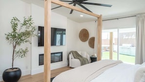 Ein Schlafzimmer mit Bett, Deckenventilator, Fernseher, Kamin, Pflanze und Balkonblick.