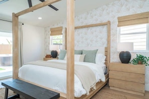 A bedroom with a four-poster bed, a wooden nightstand, a bench, and a window with blinds.